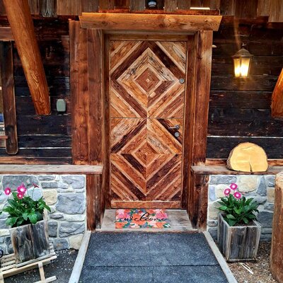 The inviting entrance of the Alm, featuring a beautifully crafted wooden door, warm lighting, and colorful flowers.