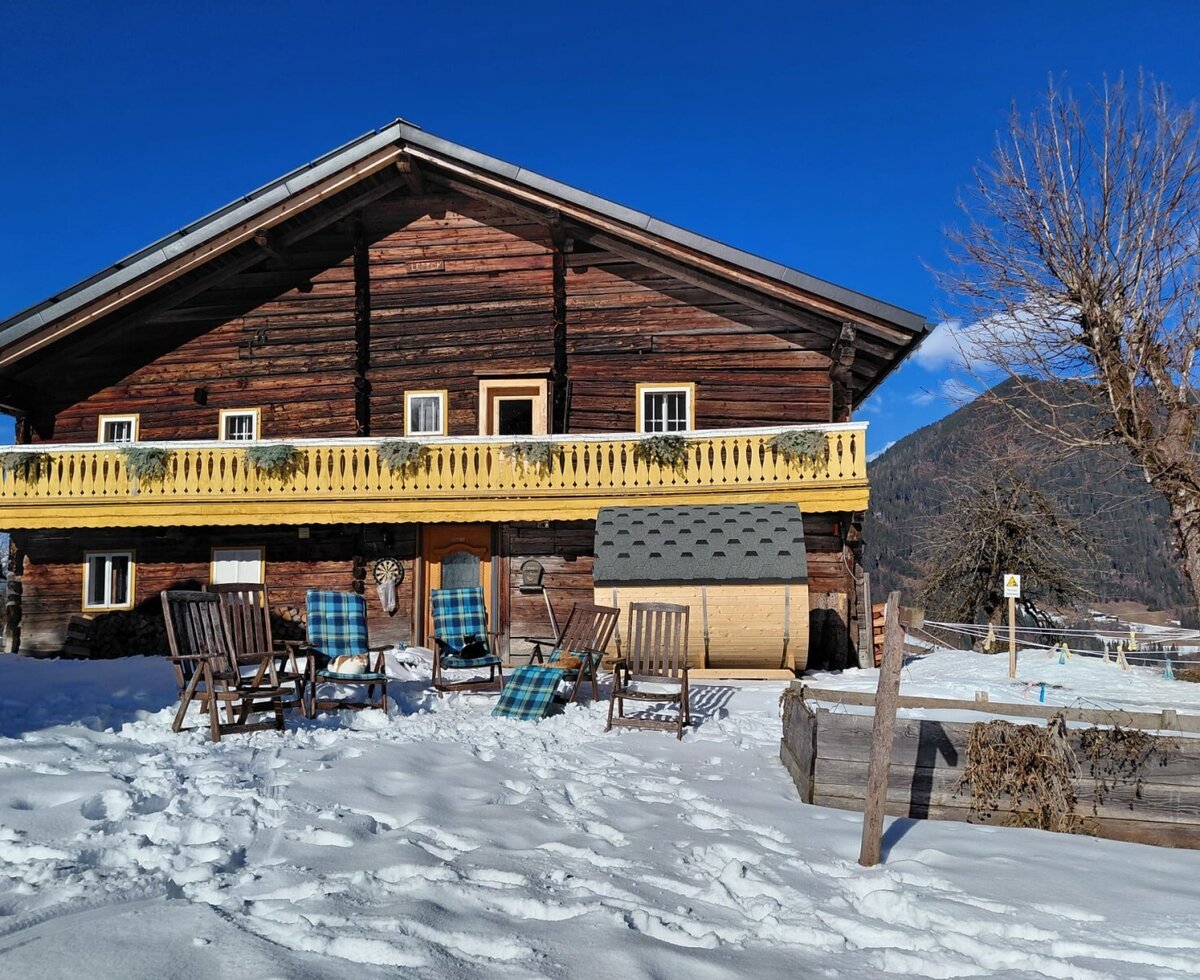 The charming bed and breakfast featuring a sunny, snow-covered terrace with cozy deck chairs and a barrel sauna against a scenic mountain backdrop.