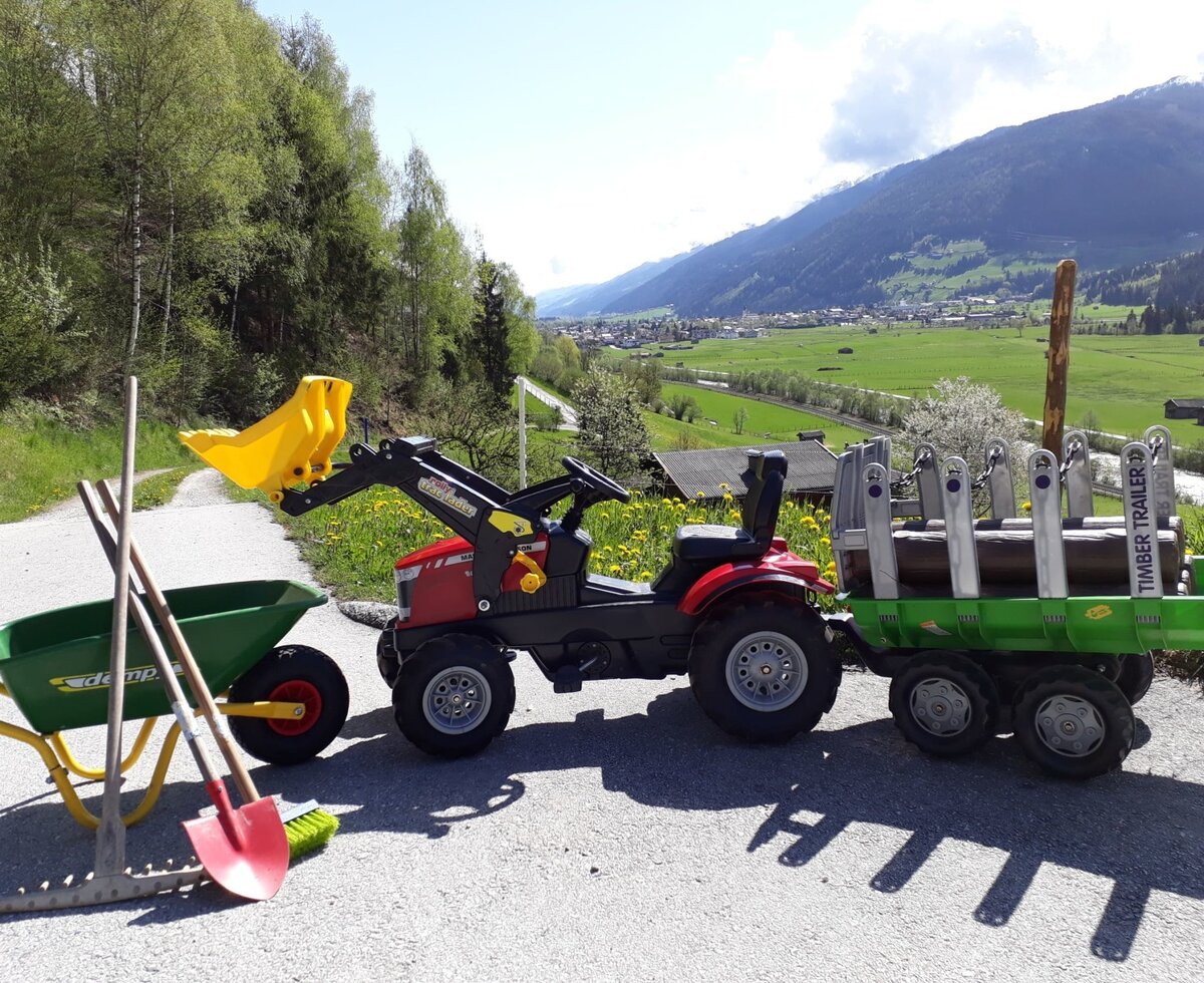 Children's play tractor with a front loader and timber trailer, alongside a wheelbarrow and play tools, available for younger guests at the Farm House.