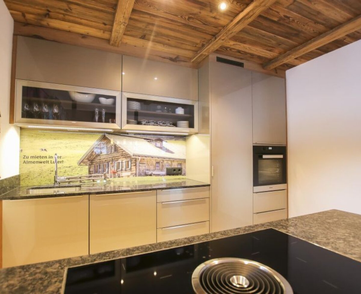 Modern kitchen in the Bed and Breakfast with an induction hob, oven, and a sink with a backsplash depicting an almhut, under a wooden ceiling.