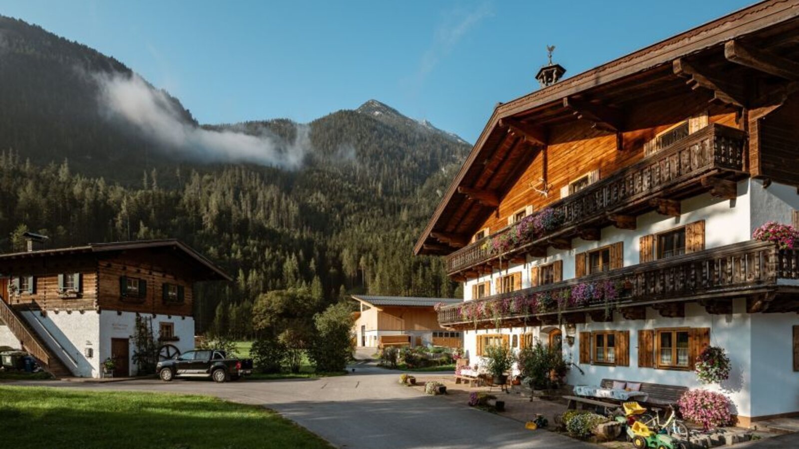 The traditional building of the organic farm with wooden balconies and flowers, surrounded by mountains and forest.