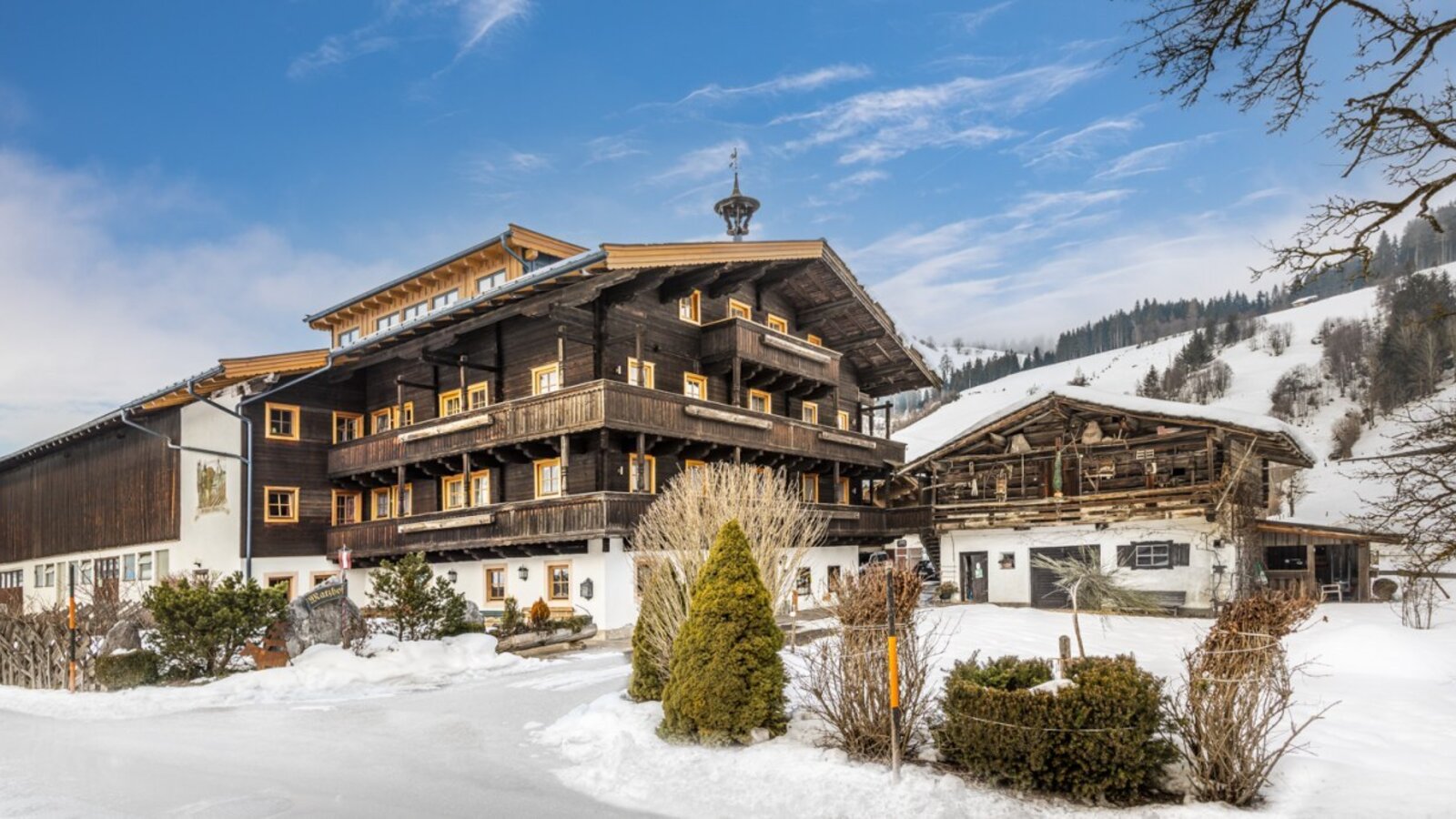 The Farm House exterior, showcasing traditional Alpine architecture with wooden balconies, set against a snow-covered landscape and distant hills.