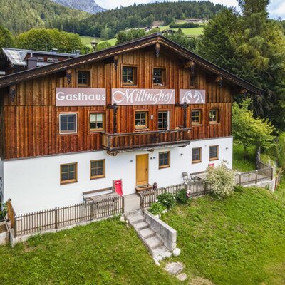 The inviting Millinghof farmhouse featuring a traditional wooden facade, surrounded by lush green lawns and forest.