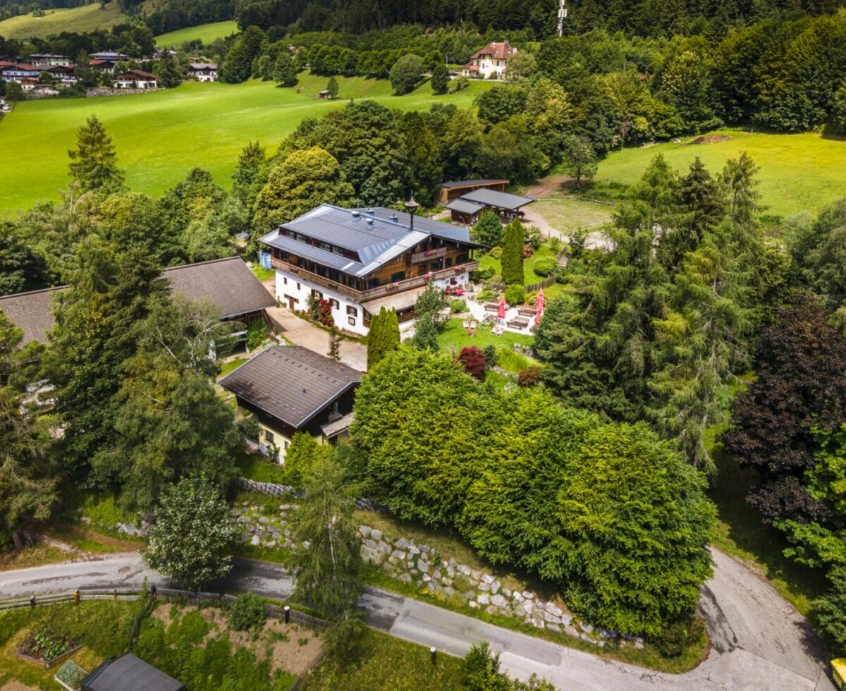 An aerial view of the idyllic farmhouse, nestled among lush green meadows and dense, vibrant forest.