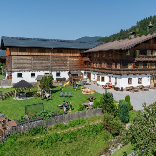 Exterior view of the farmhouse featuring a large garden, children's playground, trampoline, covered seating area, and animal enclosures.
