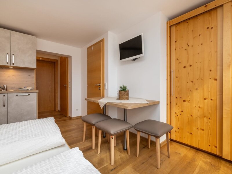 Living area of the holiday apartment at the farmhouse, featuring a kitchenette, dining table, TV, and wooden wardrobe.