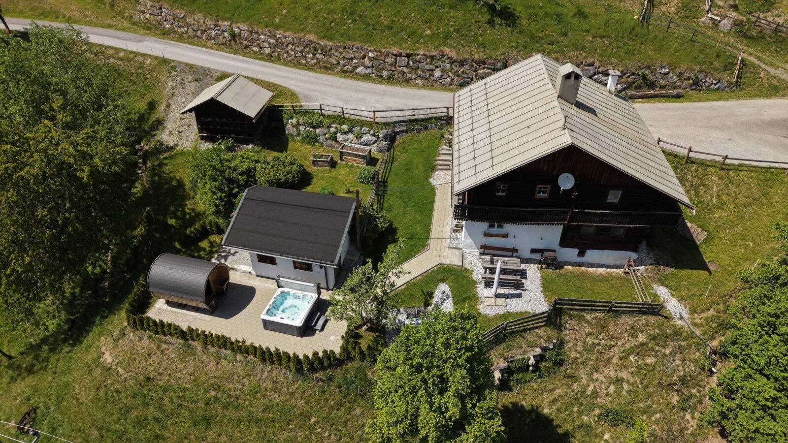 An aerial view of the idyllic Alm featuring an inviting outdoor sauna and a modern hot tub in the manicured garden area.