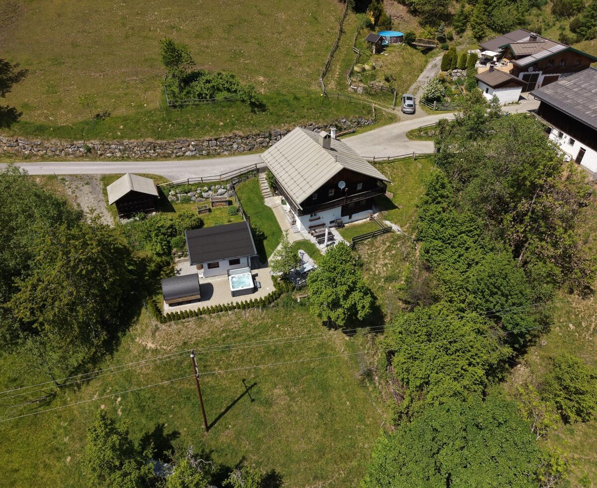 An aerial view of the idyllic Alm, surrounded by lush green meadows and featuring a private outdoor area with a hot tub.