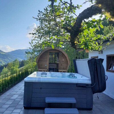 An inviting hot tub on the alm's paved terrace, featuring a wooden barrel sauna and scenic views of the surrounding mountains.
