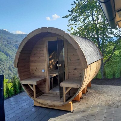 An inviting barrel sauna on the terrace of the Alm, offering scenic views of the surrounding mountains.