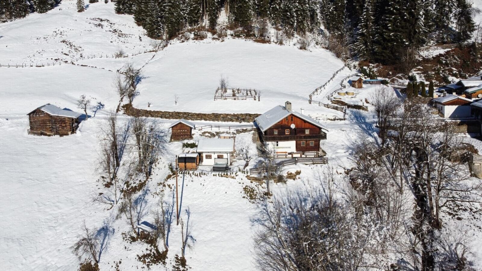 The cozy Alm nestled idyllically in a sunny, snow-covered mountain landscape.