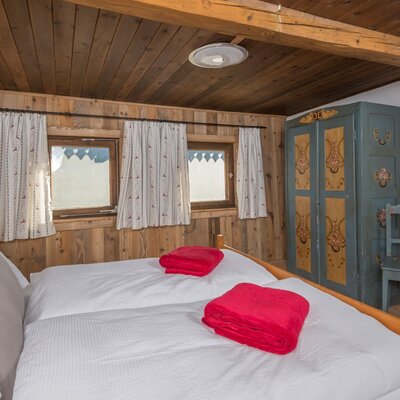 A cozy bedroom in the alm featuring rustic wooden walls, a double bed, and painted traditional furniture.
