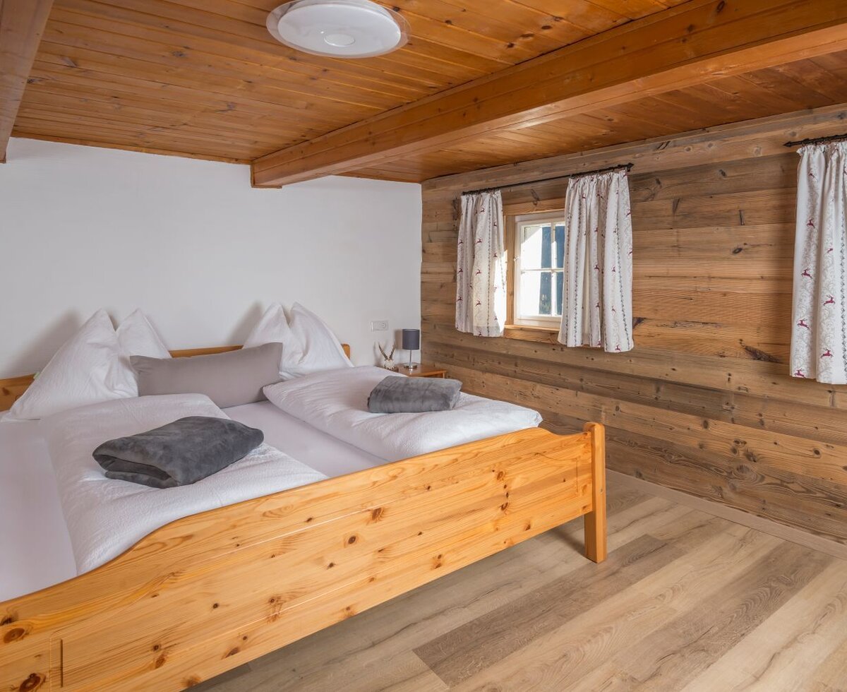 A cozy bedroom in the Alm featuring a rustic wooden double bed and traditional wood-paneled walls.
