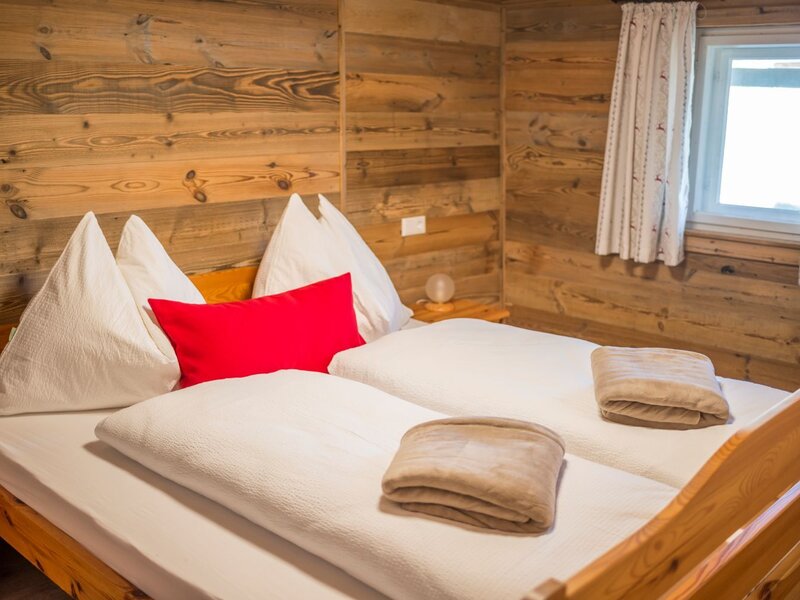 A cozy bedroom in the Alm featuring rustic wooden walls, a comfortable double bed, and soft bedding.