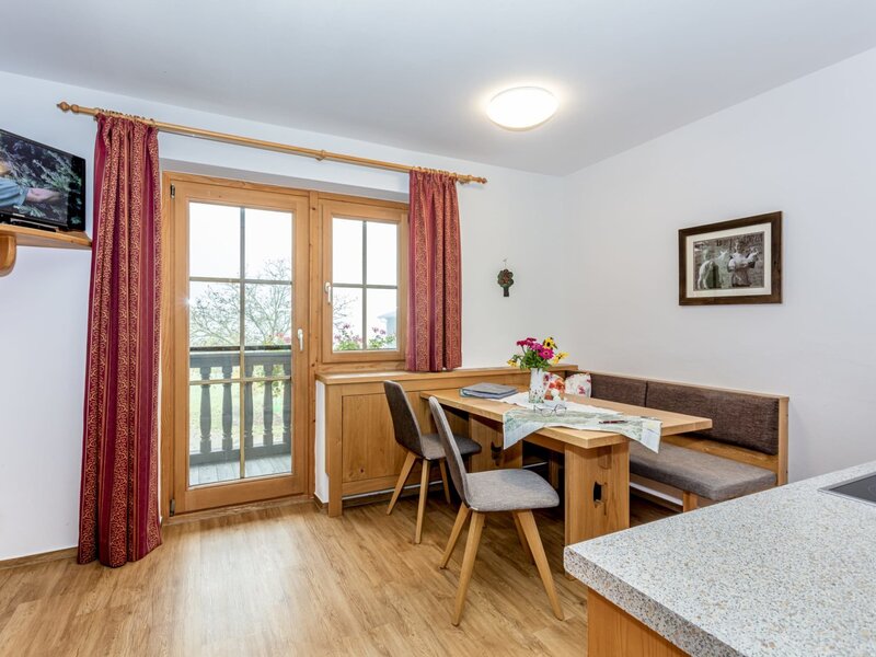 Dining area in the Farm House apartment, featuring a wooden table with bench seating, two chairs, a cable TV, and balcony access.