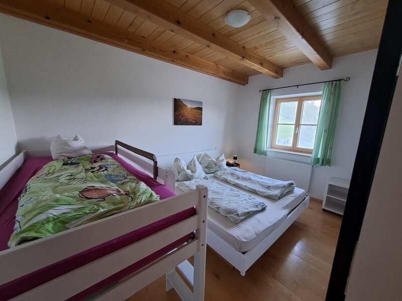 Bedroom in the holiday apartment with a double bed, a loft bed for children, and a view of the greenery