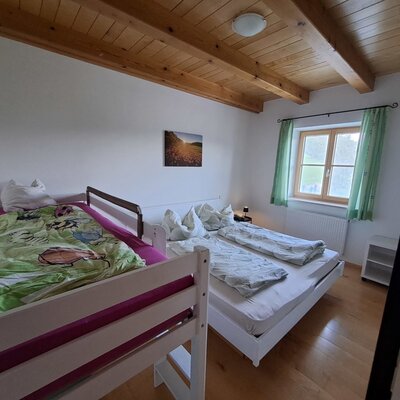 Bedroom in the holiday apartment with a double bed, a loft bed for children, and a view of the greenery