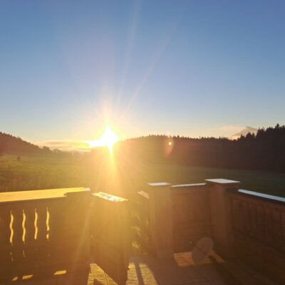 View from the balcony of the holiday apartment of the sunrise over fields, forest, and mountains.