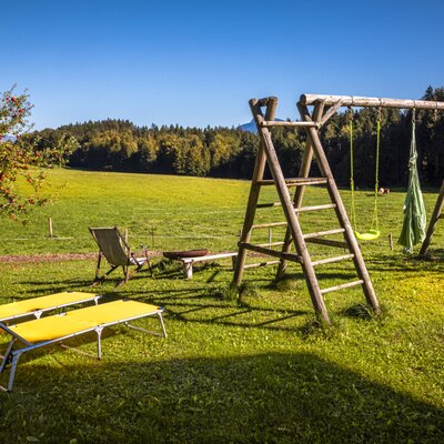 The farmhouse's spacious garden features comfortable sun loungers, a wooden playground, and scenic views of the surrounding fields.
