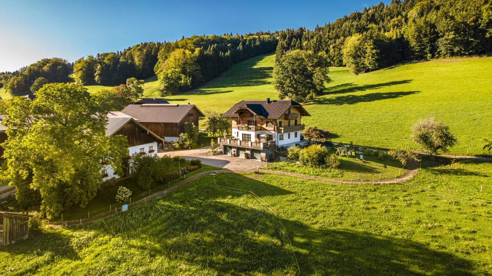 The idyllic farmhouse nestled amidst lush green meadows and rolling hills under a clear blue sky.