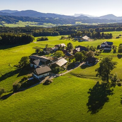 An aerial view of the inviting farmhouse, nestled amidst lush green meadows and a picturesque hilly landscape.