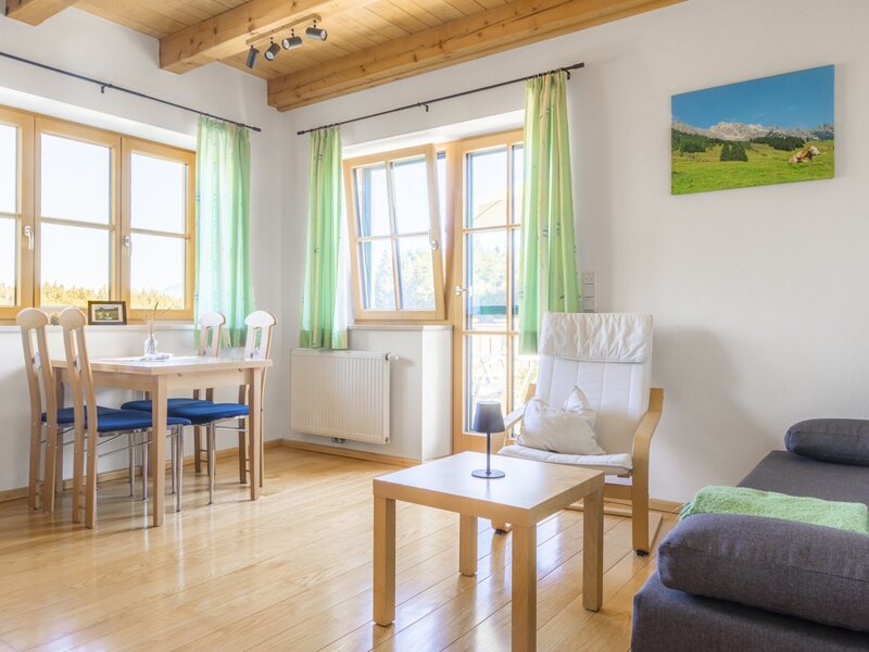 A bright and sunlit living and dining area in the farmhouse featuring comfortable seating, warm wooden accents, and large windows.