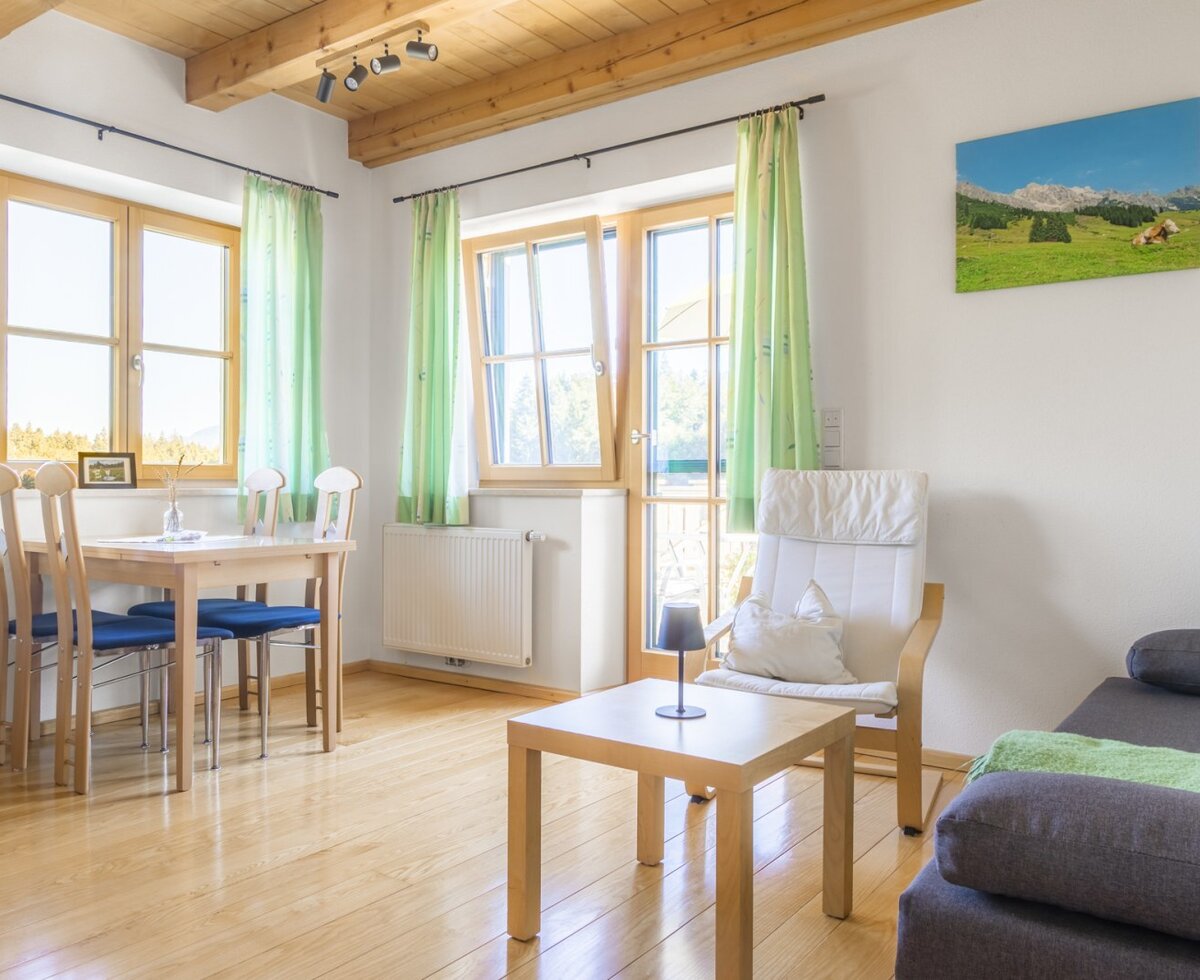 A bright and sunlit living and dining area in the farmhouse featuring comfortable seating, warm wooden accents, and large windows.