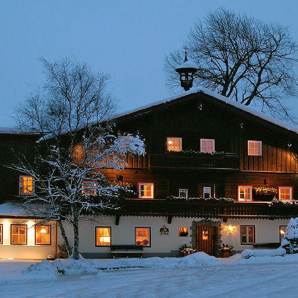 The snow-covered farm house exterior at dusk, with illuminated windows suggesting a welcoming interior.