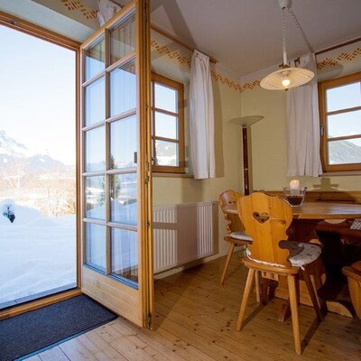 Farm House dining area with a wooden table and bench seating, providing direct access to a snowy mountain landscape.