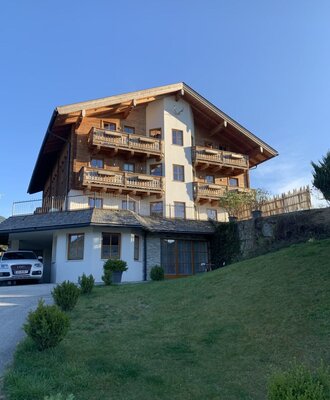 The exterior of the multi-story farm house features wooden balconies on upper levels and a carport on the ground floor.