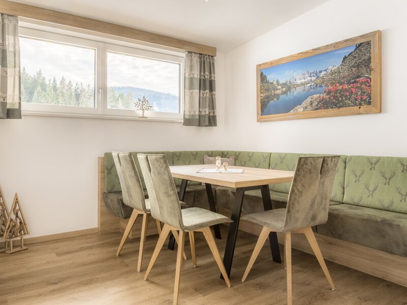 Dining area of the apartment in the farmhouse with a wooden table, bench, chairs, and a window with mountain views.