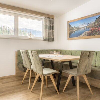Dining area of the apartment in the farmhouse with a wooden table, bench, chairs, and a window with mountain views.