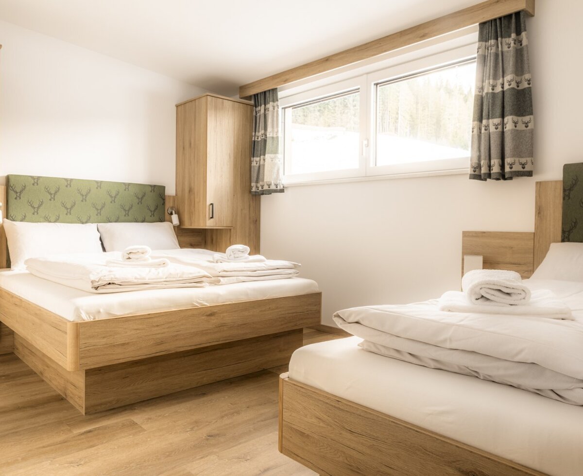 Bedroom with a double bed, a single bed, wooden furniture, and a window.
