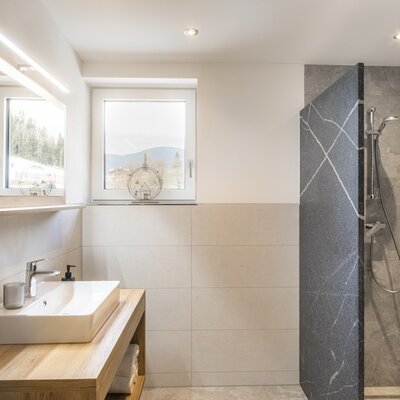 Modern bathroom with a sink on a wooden vanity, illuminated mirror, walk-in shower, and window with mountain view.