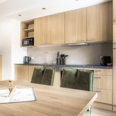 Modern kitchen with wooden elements, a dining table, green chairs, and kitchen appliances such as a microwave and coffee machine.