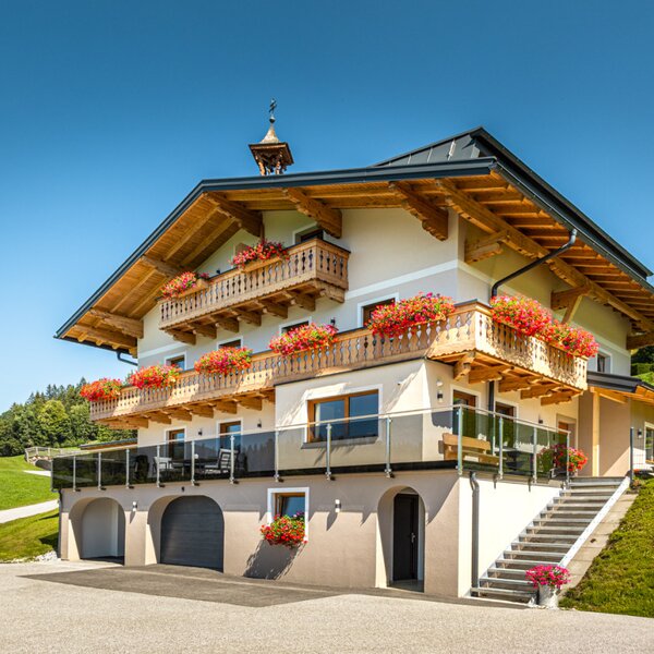 The inviting farmhouse featuring traditional wooden balconies adorned with vibrant flowers, surrounded by lush green meadows.