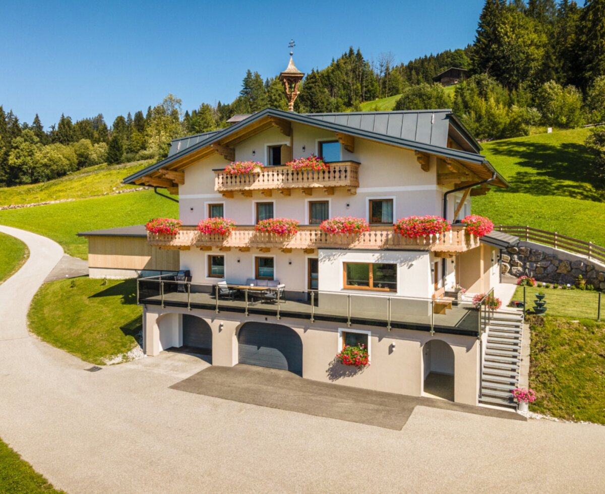 The inviting Peterlehen farmhouse in an idyllic, sunny hillside location with flower-filled balconies and expansive green meadows.