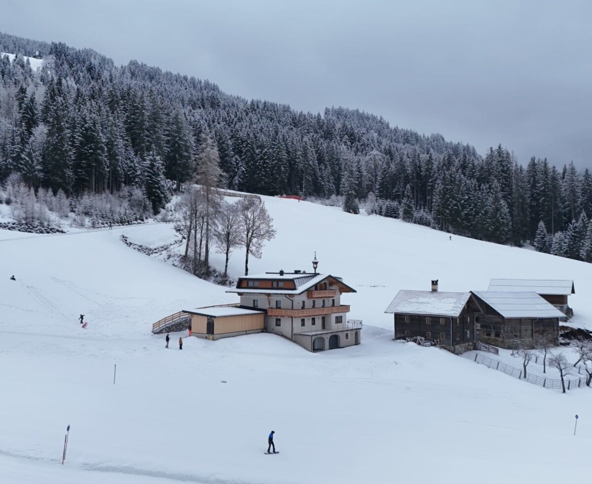 The idyllic farmhouse nestled in a snowy winter landscape, located directly by the ski slope and surrounded by snow-covered pine forests.