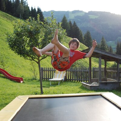 The farmhouse offers an outdoor play area with a trampoline, a red slide, and a sandbox, surrounded by green hills.