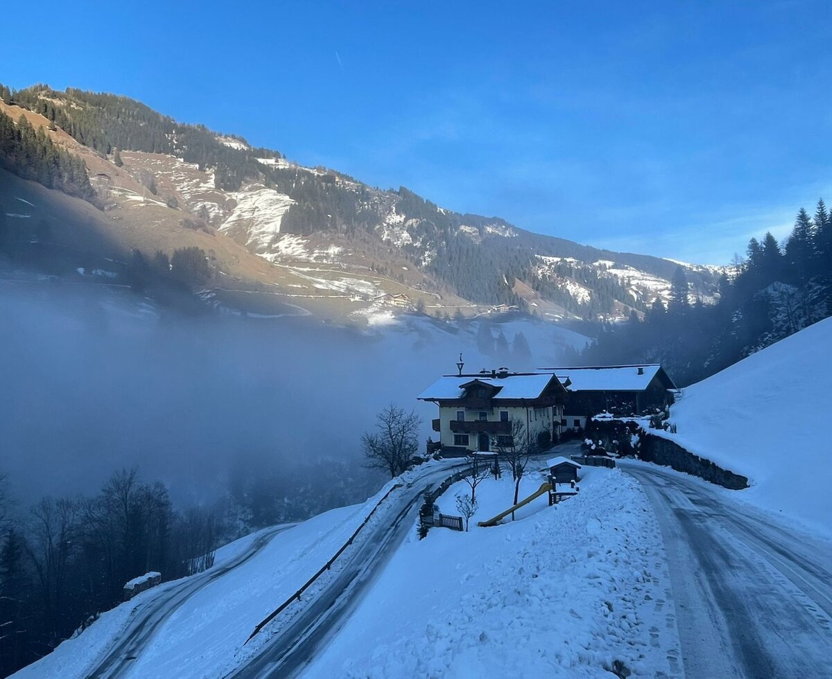 The Farm House set in a snowy mountain valley, with a clear road leading to the property and distant fog.