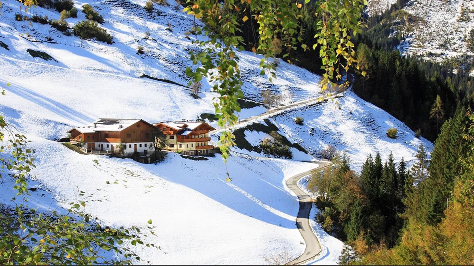 The farmhouse surrounded by snow-covered slopes and an access road.