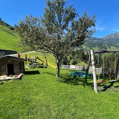 The farmhouse offers an outdoor play area with a sandpit, swings, slide, trampoline, and a children's playhouse on a grassy lawn.