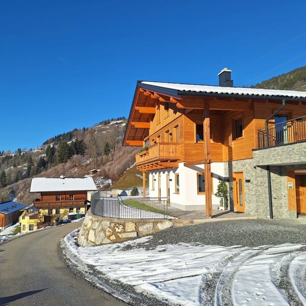 Exterior view of the farmhouse with a wooden facade, stone elements, and a garage, surrounded by snowy hills.