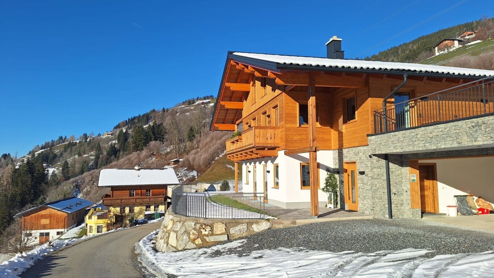 Exterior view of the farmhouse with a wooden facade, stone elements, and a garage, surrounded by snowy hills.