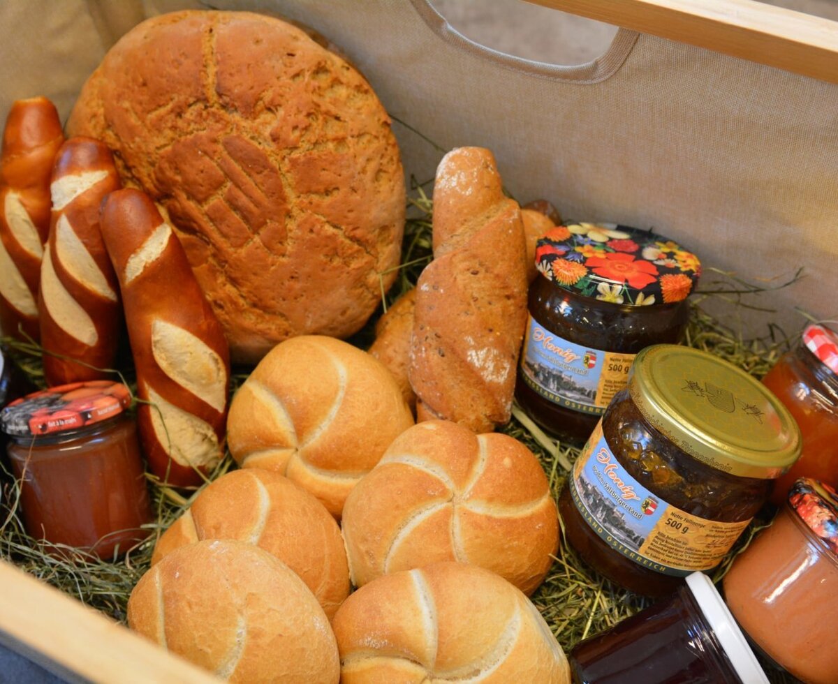 A selection of fresh bread, pretzels, rolls, and various jams, presented in a basket at the farmhouse.