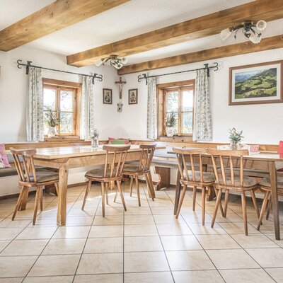 The farmhouse dining area with wooden tables, chairs, bench seating, and exposed ceiling beams.