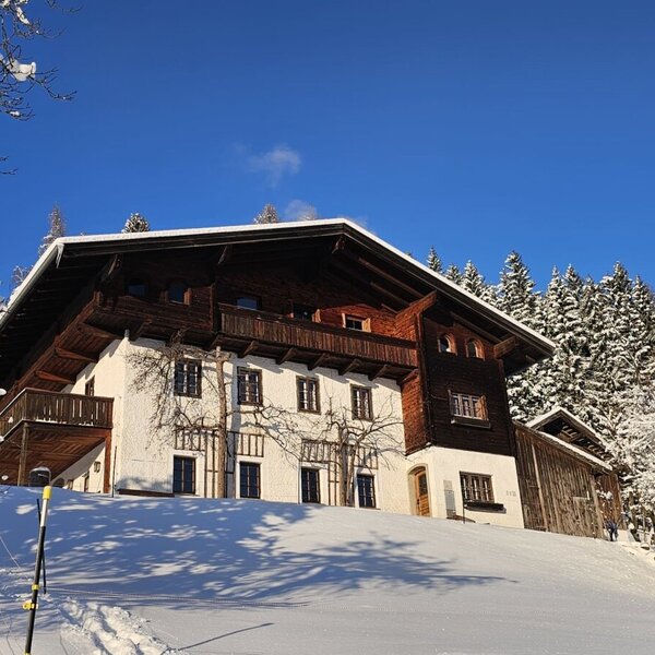 The farmhouse in a winter landscape with snow and snow-covered trees under a clear blue sky.