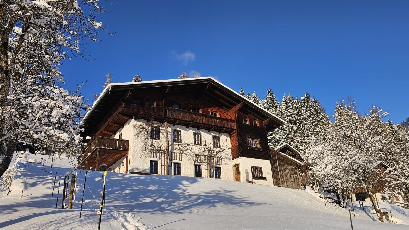 The farmhouse in a winter landscape with snow and snow-covered trees under a clear blue sky.