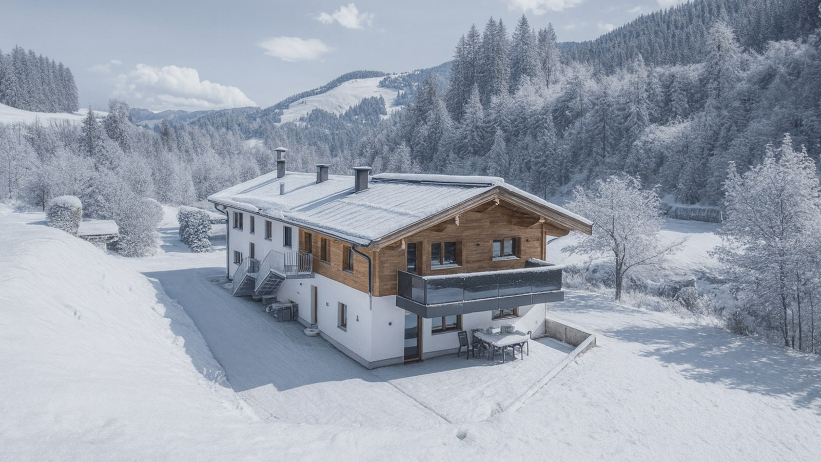 The farmhouse in winter, with snow-covered mountains and trees in the background, features a balcony and a patio with seating.