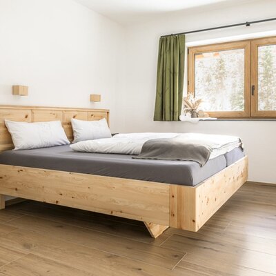 Bedroom featuring a wooden bed, a floating nightstand, and a window with a view of trees.
